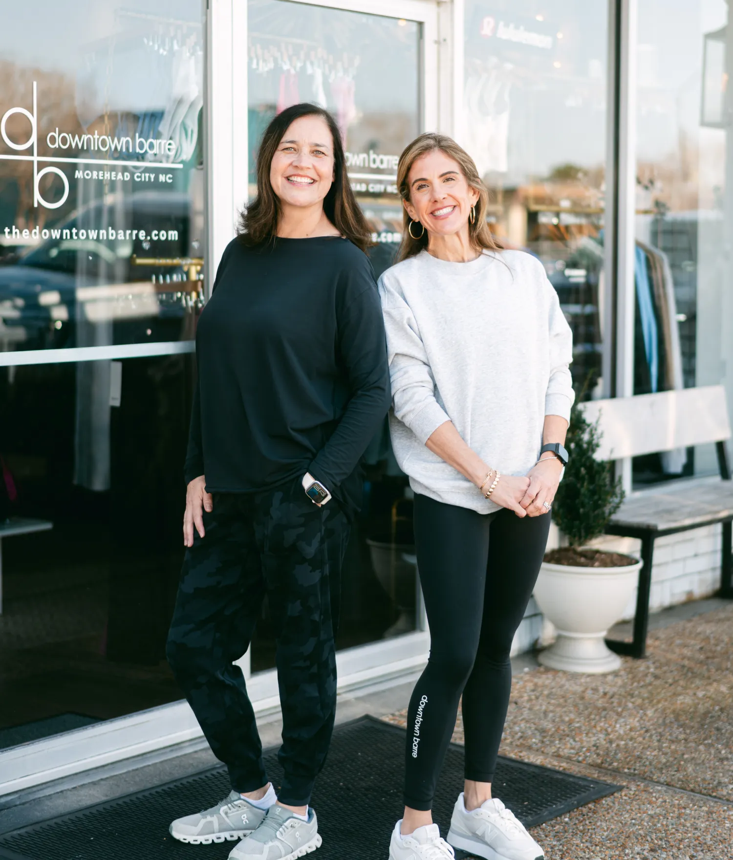ABoutusAnna and Sam-2 Two women in casual athletic wear smile while standing outside a fitness studio.