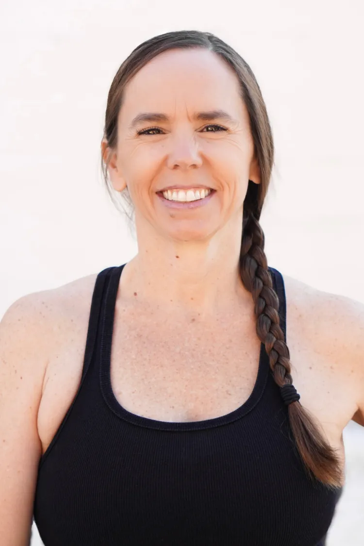 Smiling woman with long brown hair in a braid, wearing a black tank top, standing against a light background.