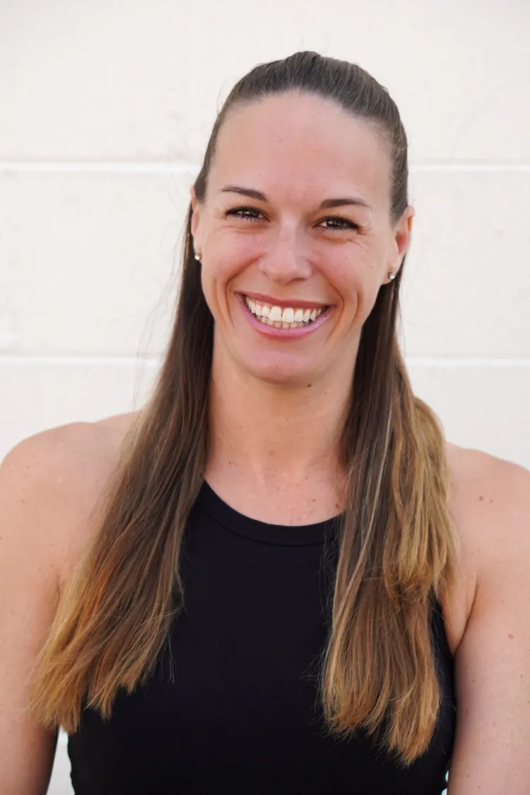 Marissa LaCarrubba Woman with long brown hair in a black tank top smiling in front of a white wall.
