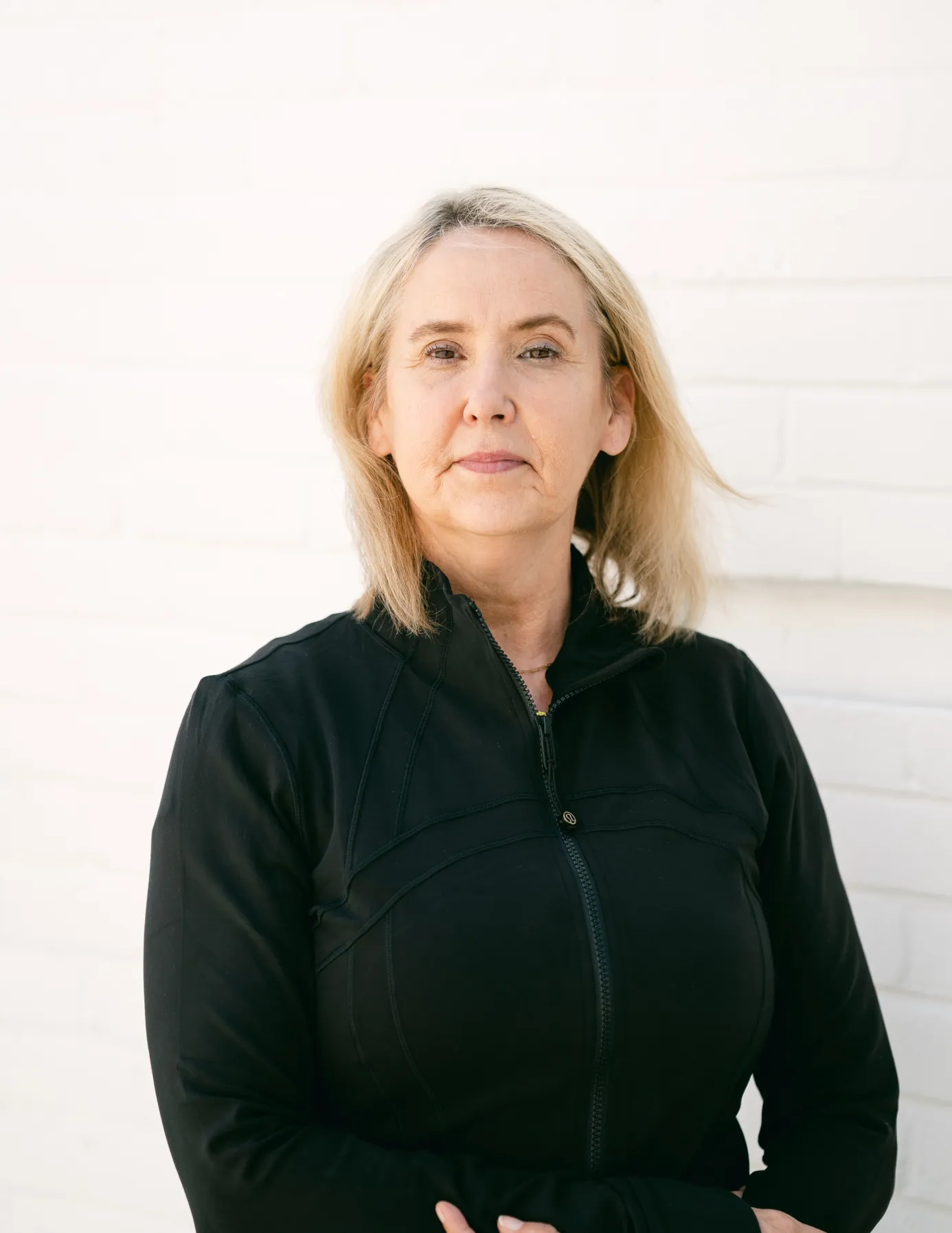 SusanWilliamsBoutiquemanager 1 A woman with blonde hair in a black jacket stands in front of a white brick wall, looking at the camera.