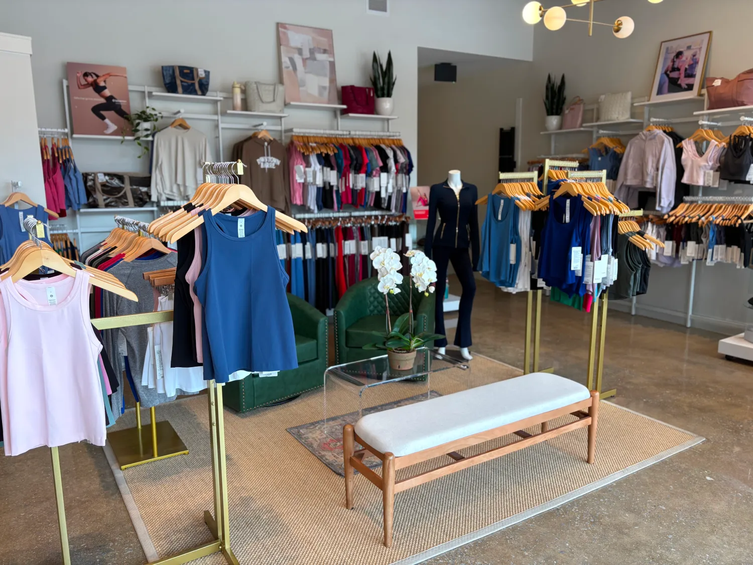 Clothing boutique with racks of colorful athletic wear, a mannequin, green chairs, and a white bench.