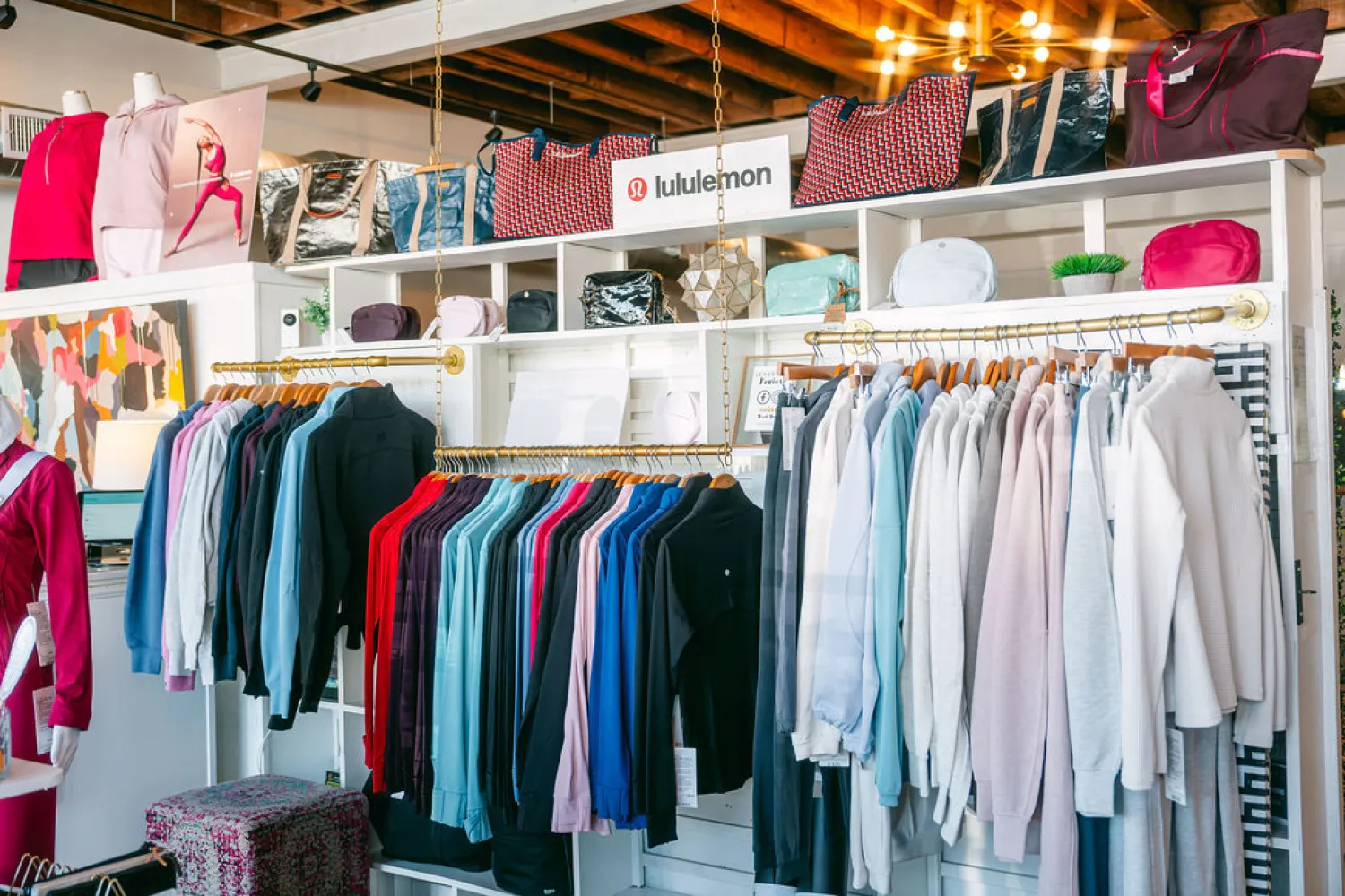 Clothing racks with colorful Lululemon tops, sweaters, and bags displayed in a bright retail store.